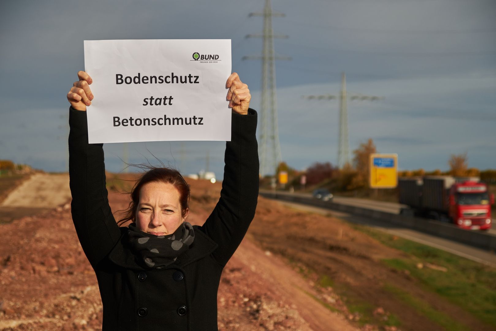Jenni Follmann BUND hält ein Schild hoch auf dem "Bodenschutz statt Betonschmutz" steht